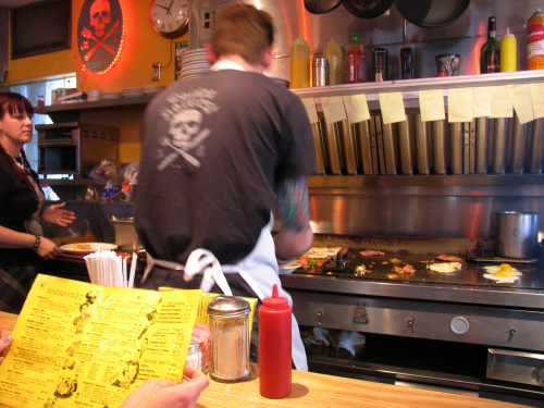 One man, one grill, one heck of a breakfast. Paige studies the menu as waitress Vanessa (left) waits for a plate from Zane, who is working his way through the line of order slips above the grill